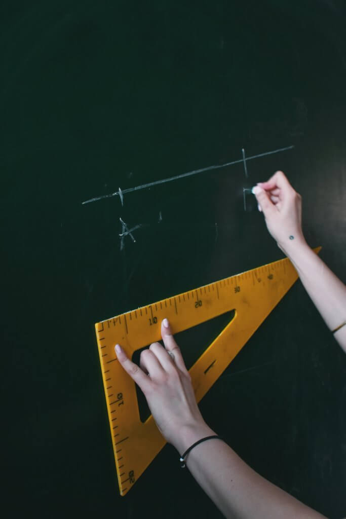 Enseignante traçant un segment à l'aide d'une équerre sur un tableau noir.